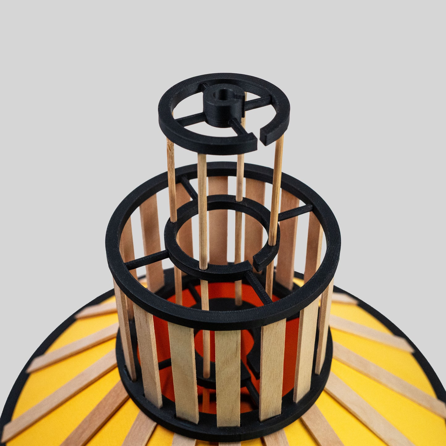 Design-lampskärm i gult med svarta delar och trädetaljer fotad snett ovanifrån