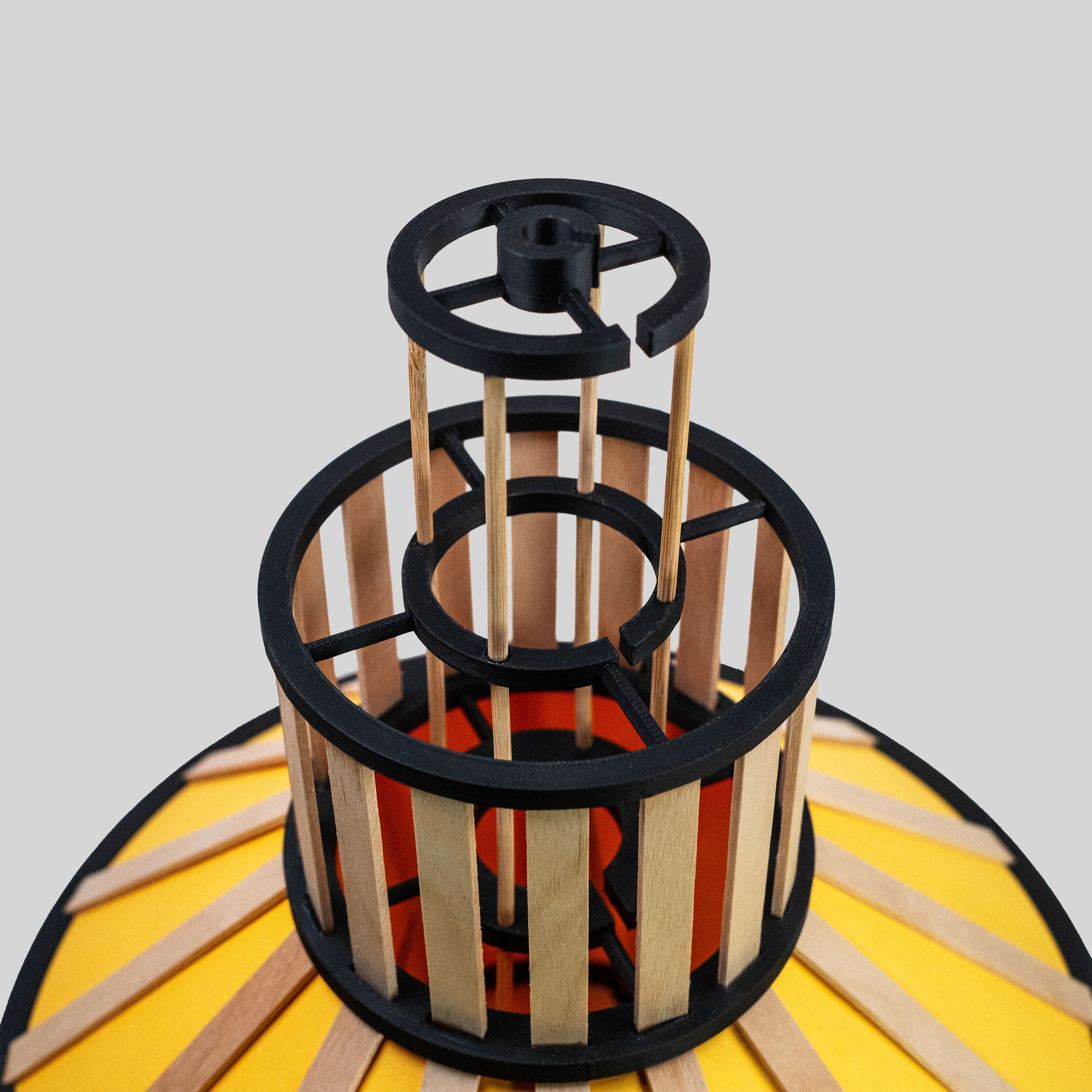 Design-lampskärm i gult med svarta delar och trädetaljer fotad snett ovanifrån